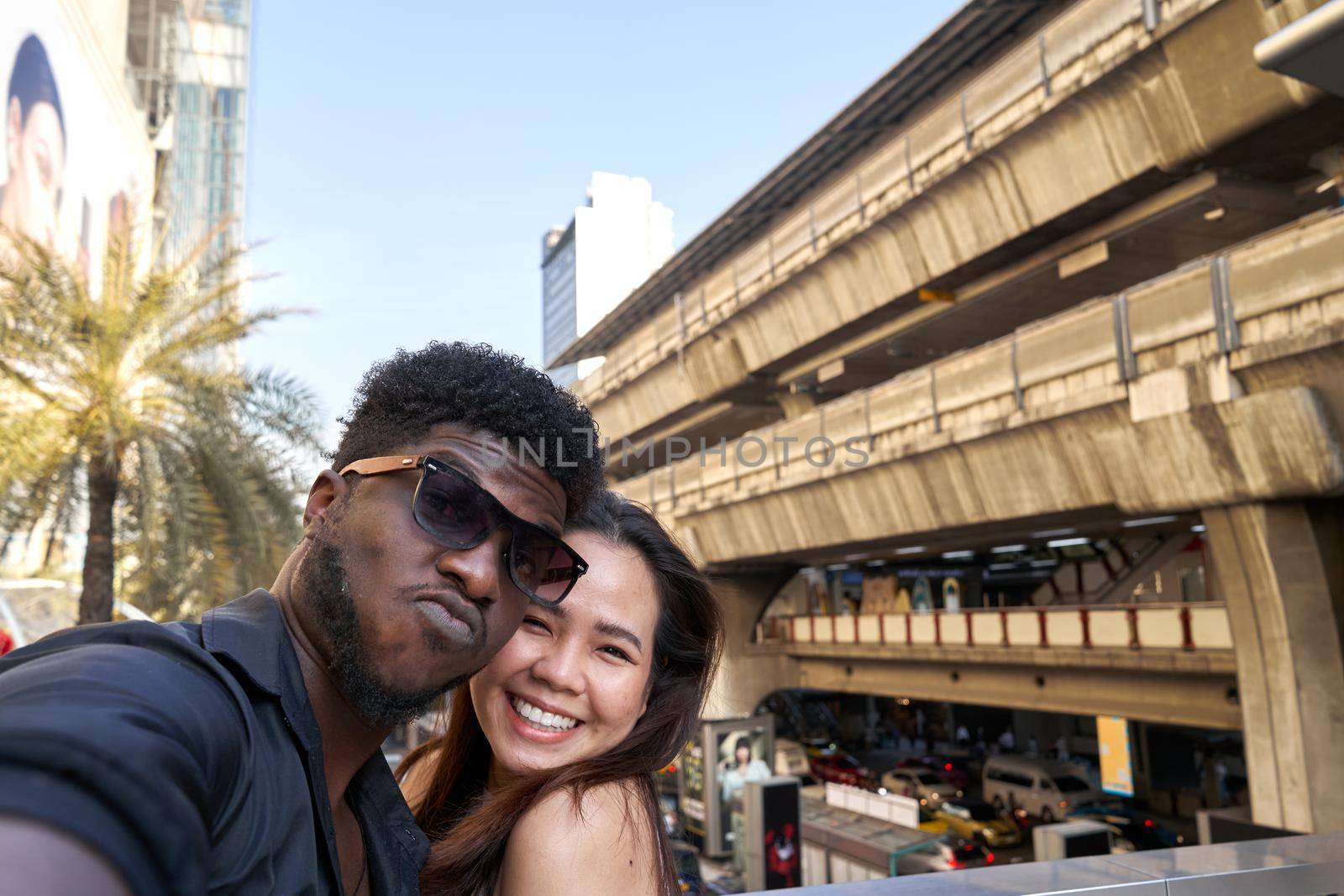 Two multiracial friends embracing while taking a selfie outside a shopping mall