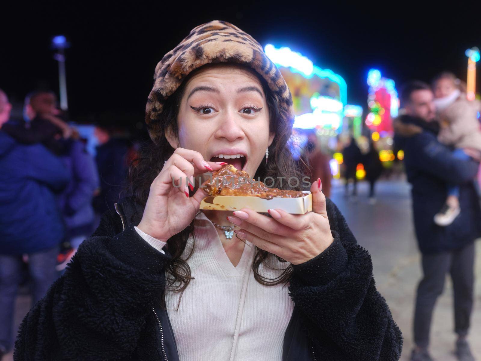 Portrait of a smiling latina woman eating a chocolate waffle with happy expression in a night fair