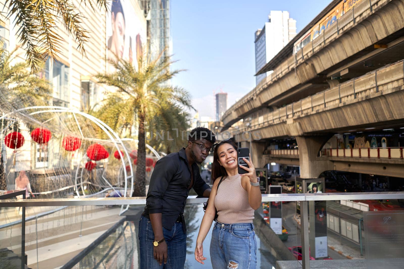 Young asian woman and african man taking a selfie outside a shopping center in Bangkok