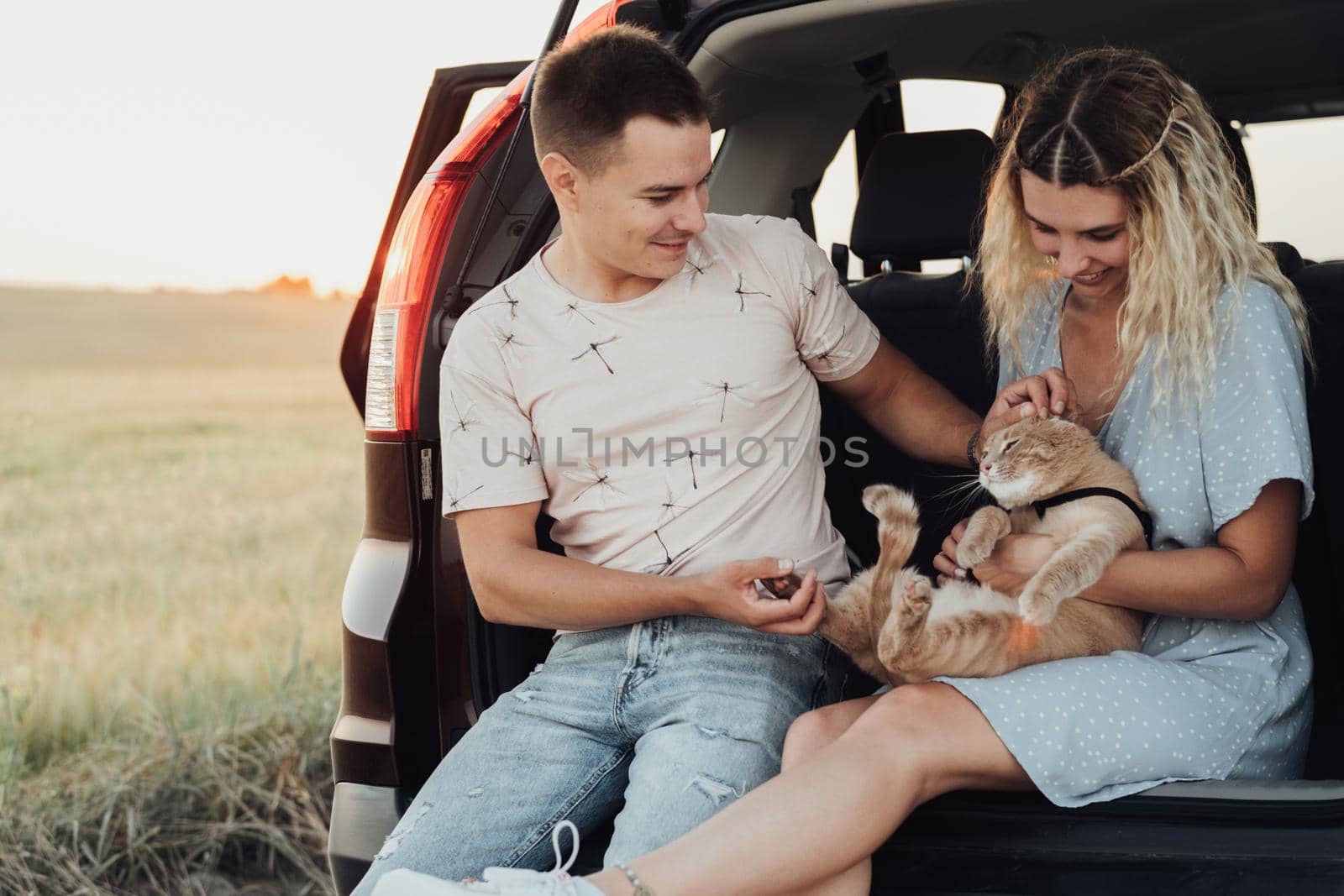 Young Woman and Man Sitting in Trunk of Car with Pet, Happy Couple with Their Red Cat Enjoying Road Trip