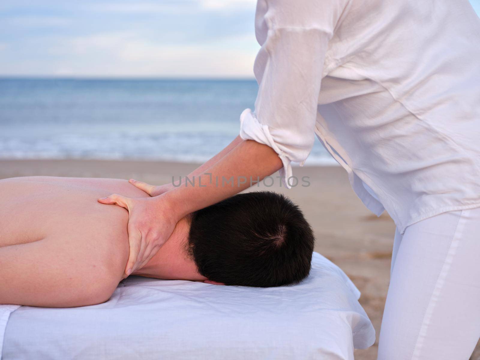 Young man receiving shoulder massage from a female chiromassage therapist on a beach in Valencia. by WesternExoticStockers