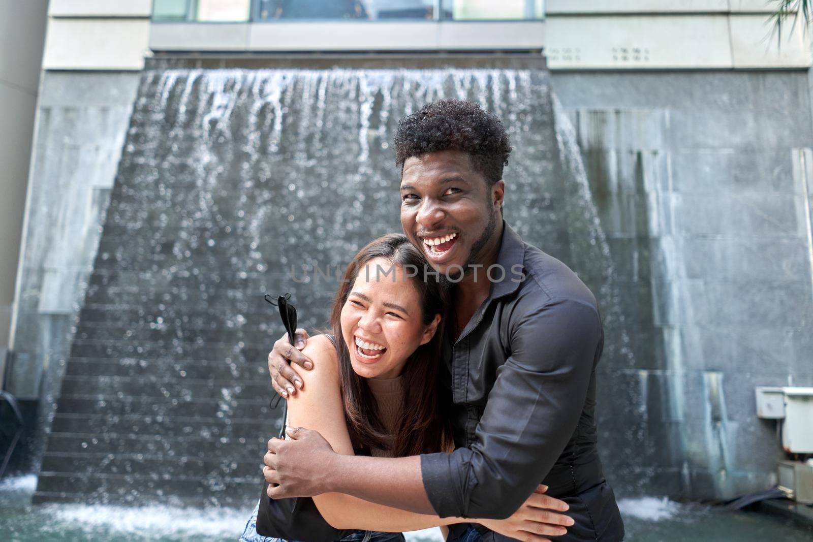 Two multiethnic friends embracing with a happy expression ouside a modern shopping mall in Thailand