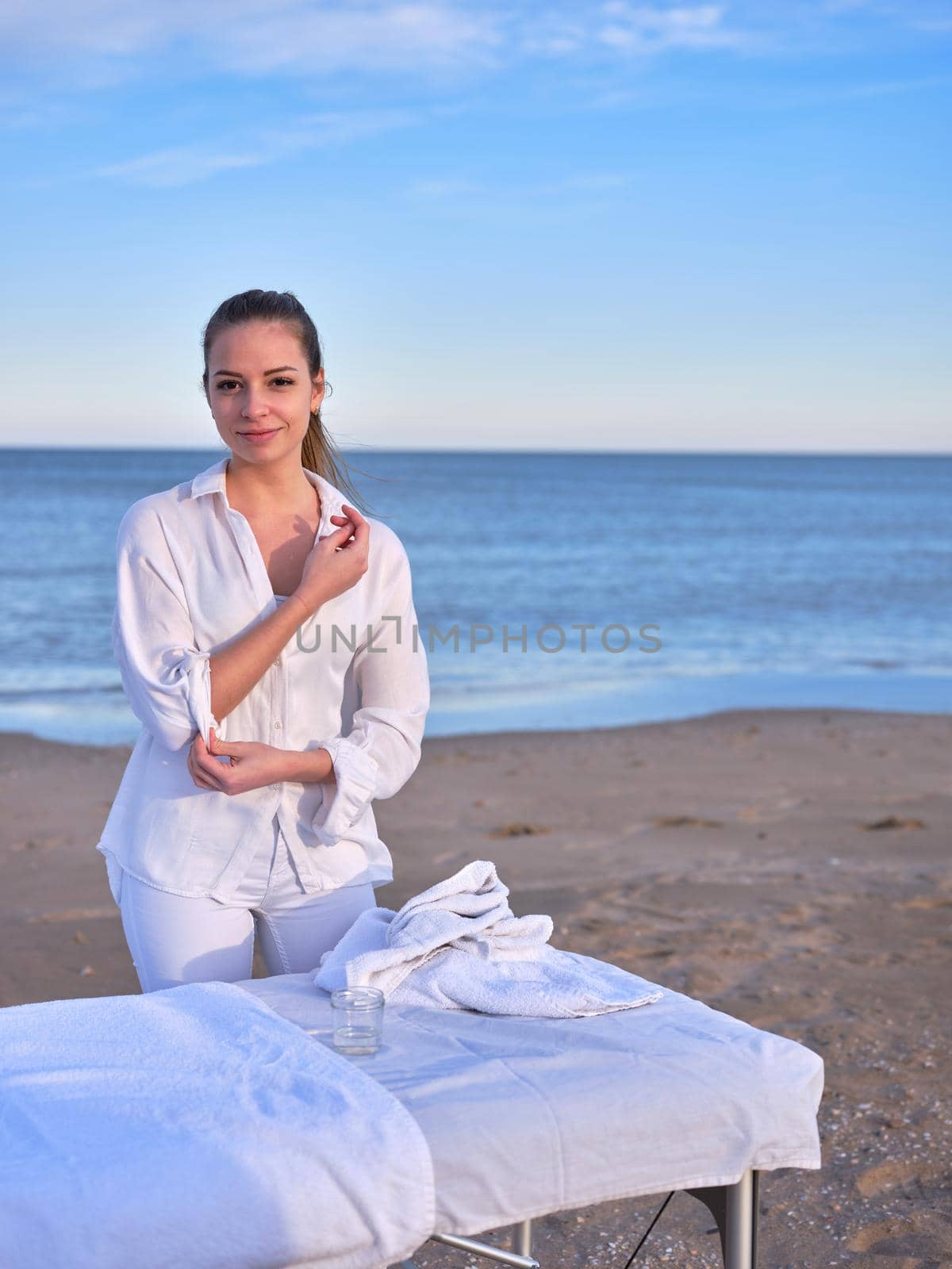 A young chiromassage therapist posing and standing near of the massage table on a beach with the sea in the background. by WesternExoticStockers