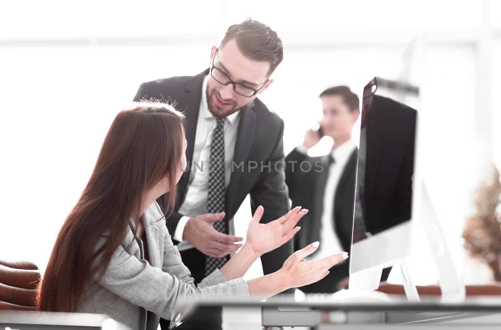 Manager talking with an employee standing near the desktop in the office