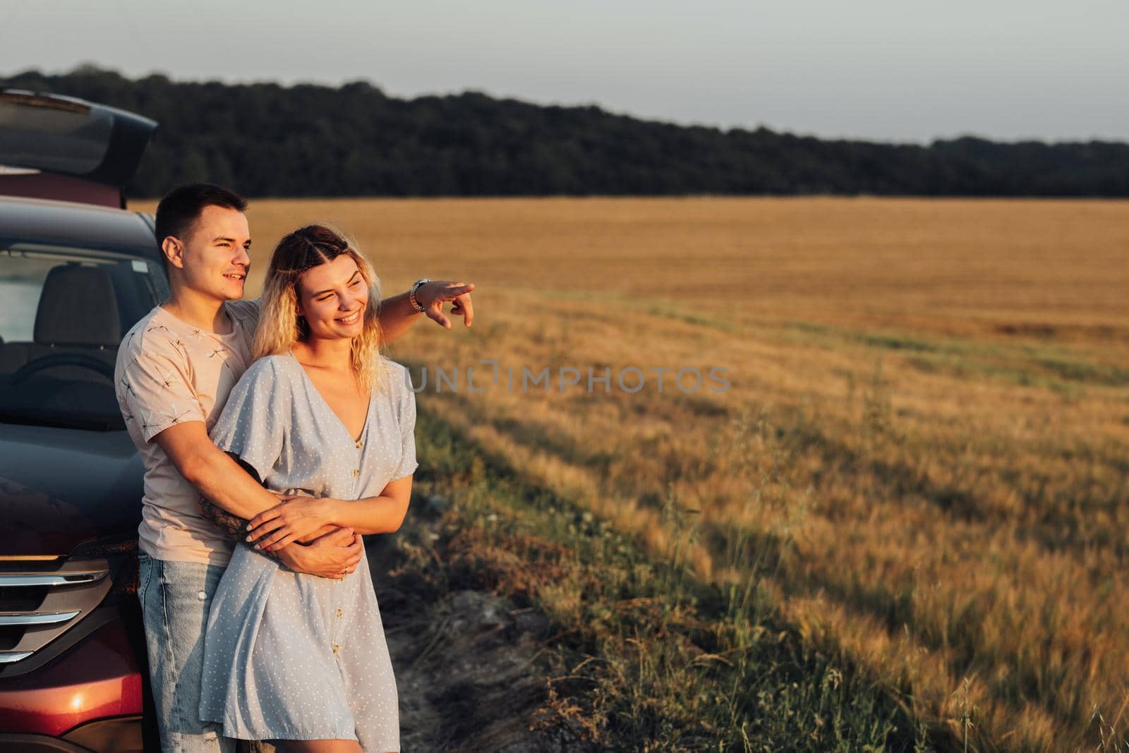 Cheerful Young Couple Hugging Near Car, Caucasian Woman and Man Enjoying Road Trip at Sunset, Copy Space