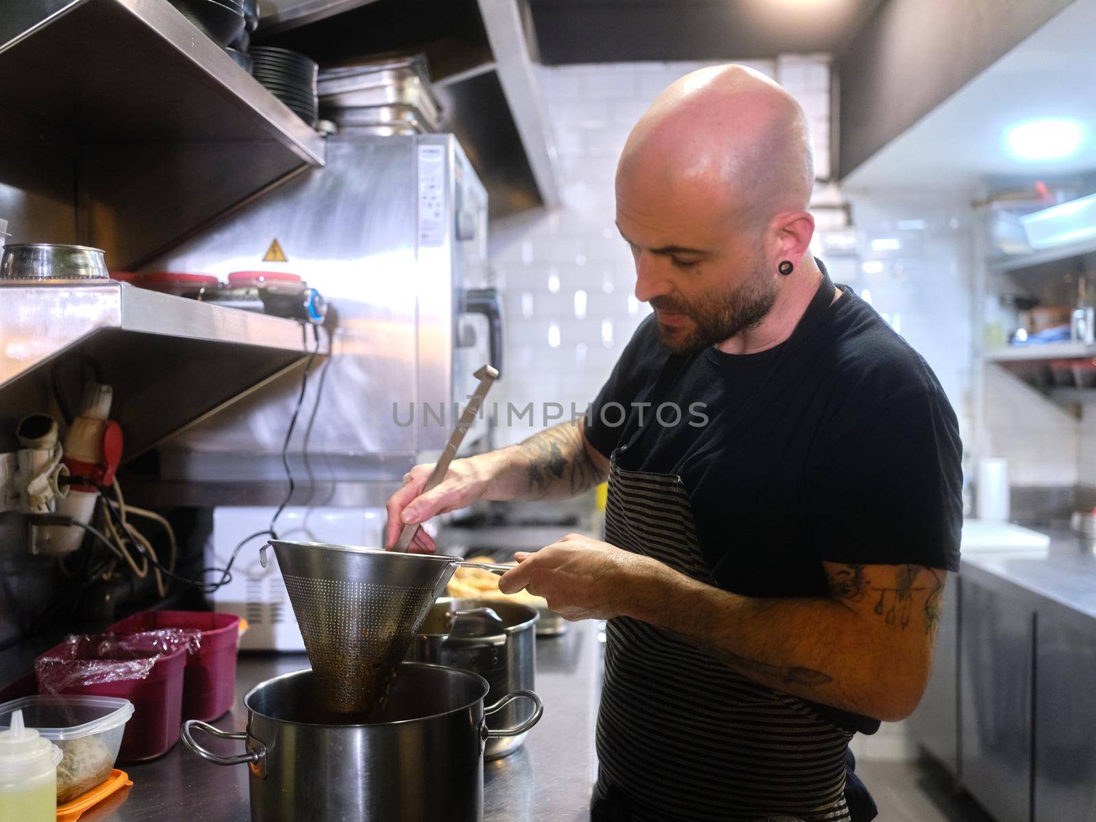 Professional cook using a colander in the kitchen of a restaurant by WesternExoticStockers