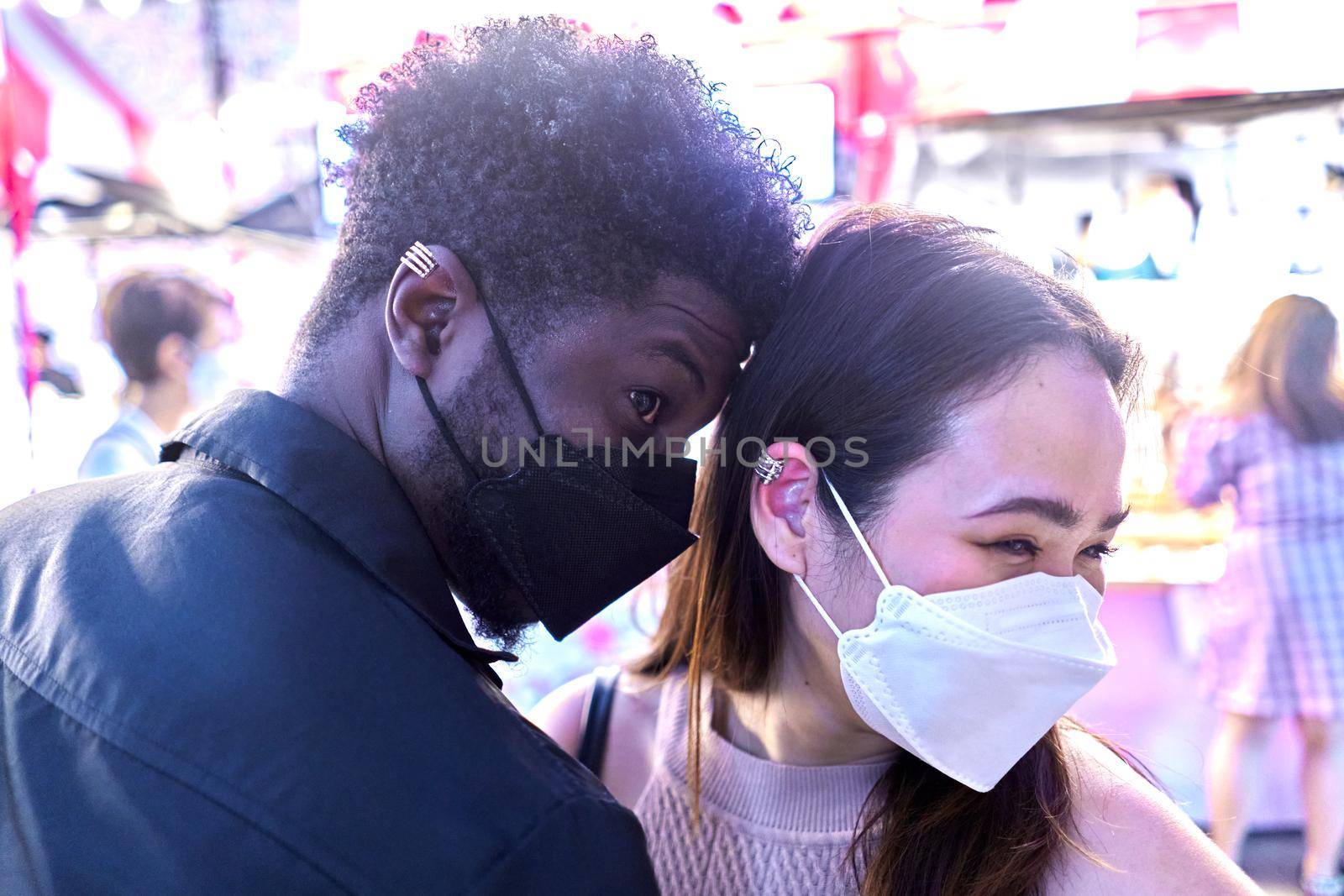Multiracial friends wearing mask showing off new earrings in their ears in a street market at night