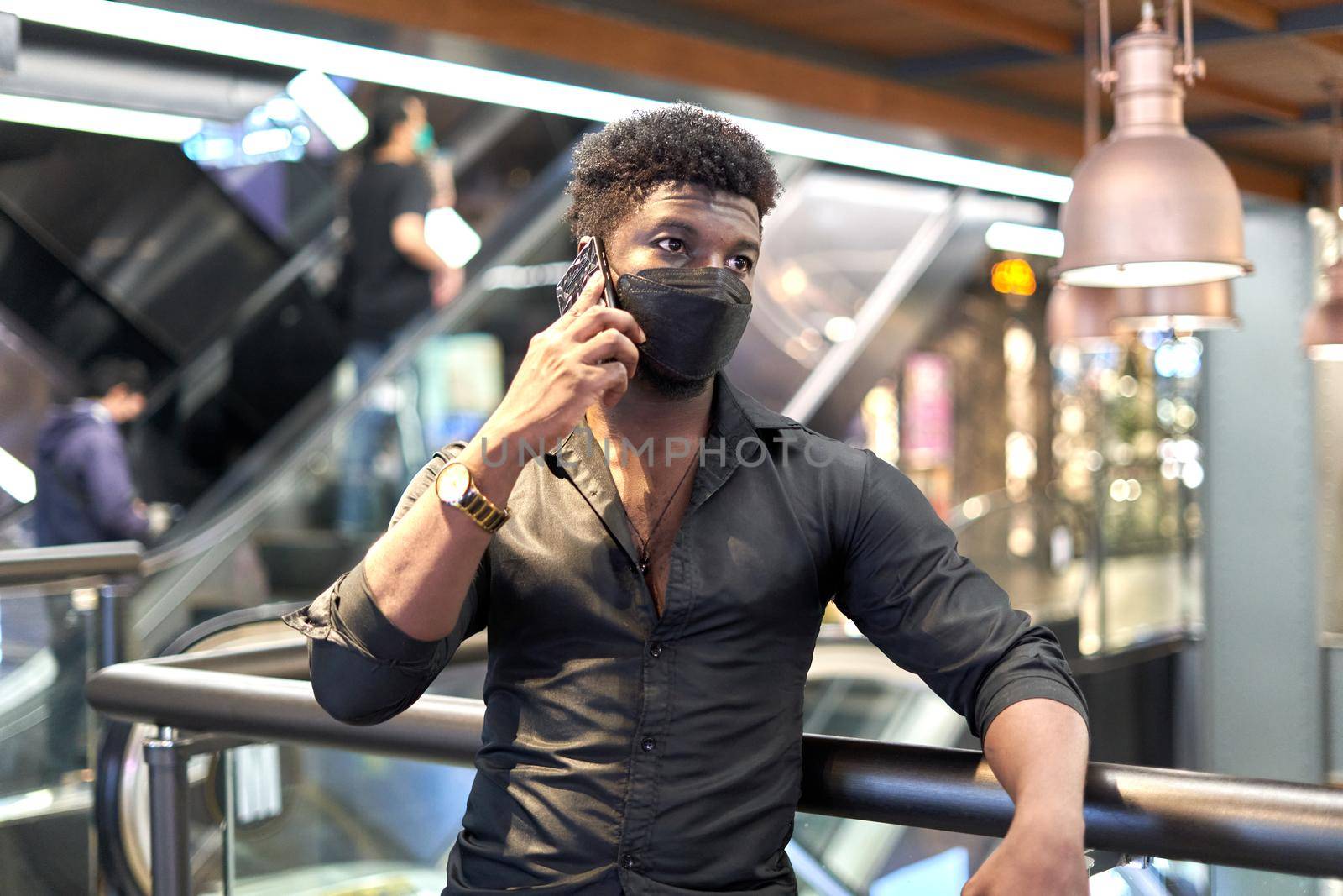 Portrait of an african man in mask talking to the mobile in a shopping mall