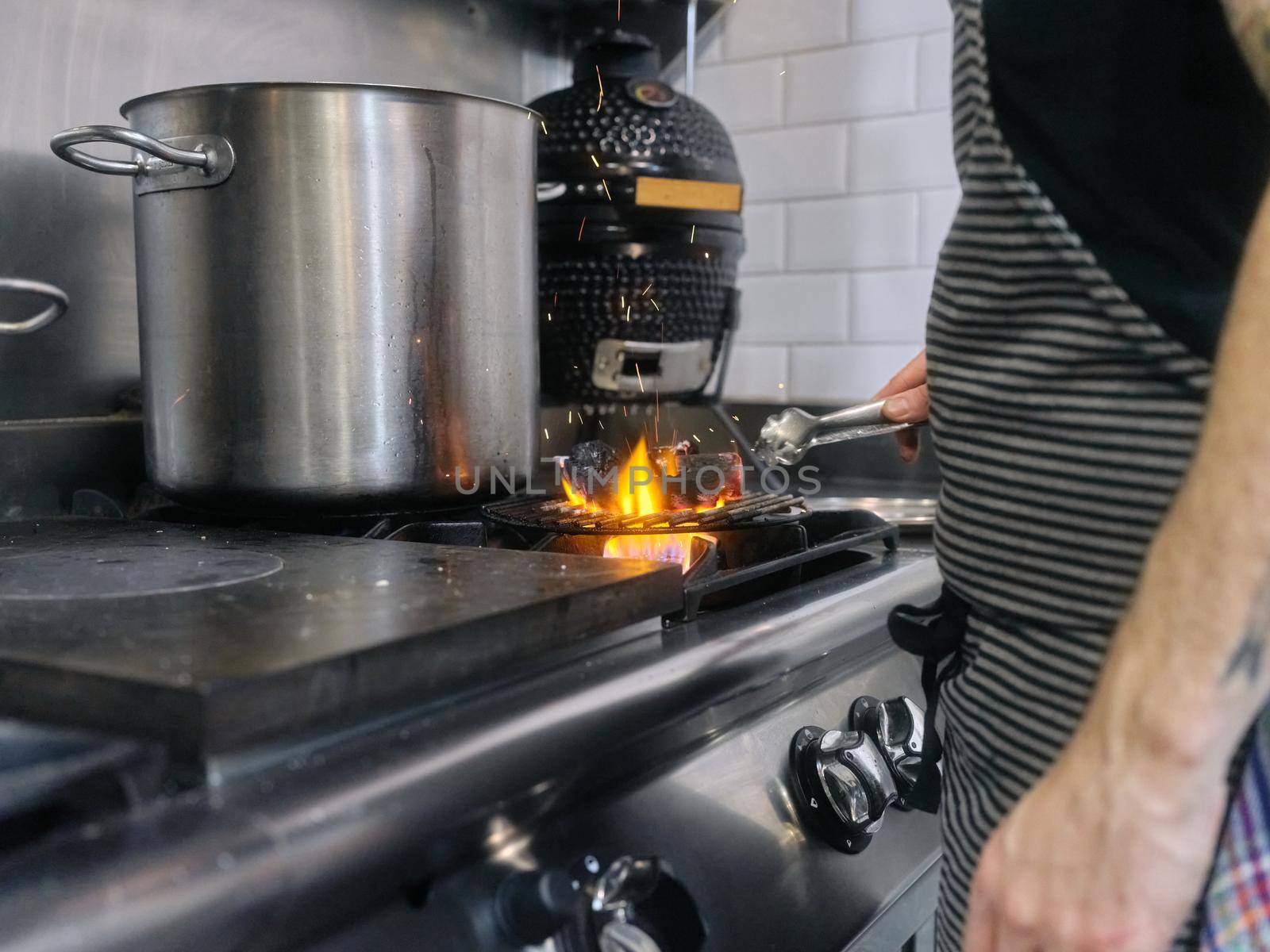 Cook using tongs to remove charcoal that is on the fire in a restaurant by WesternExoticStockers