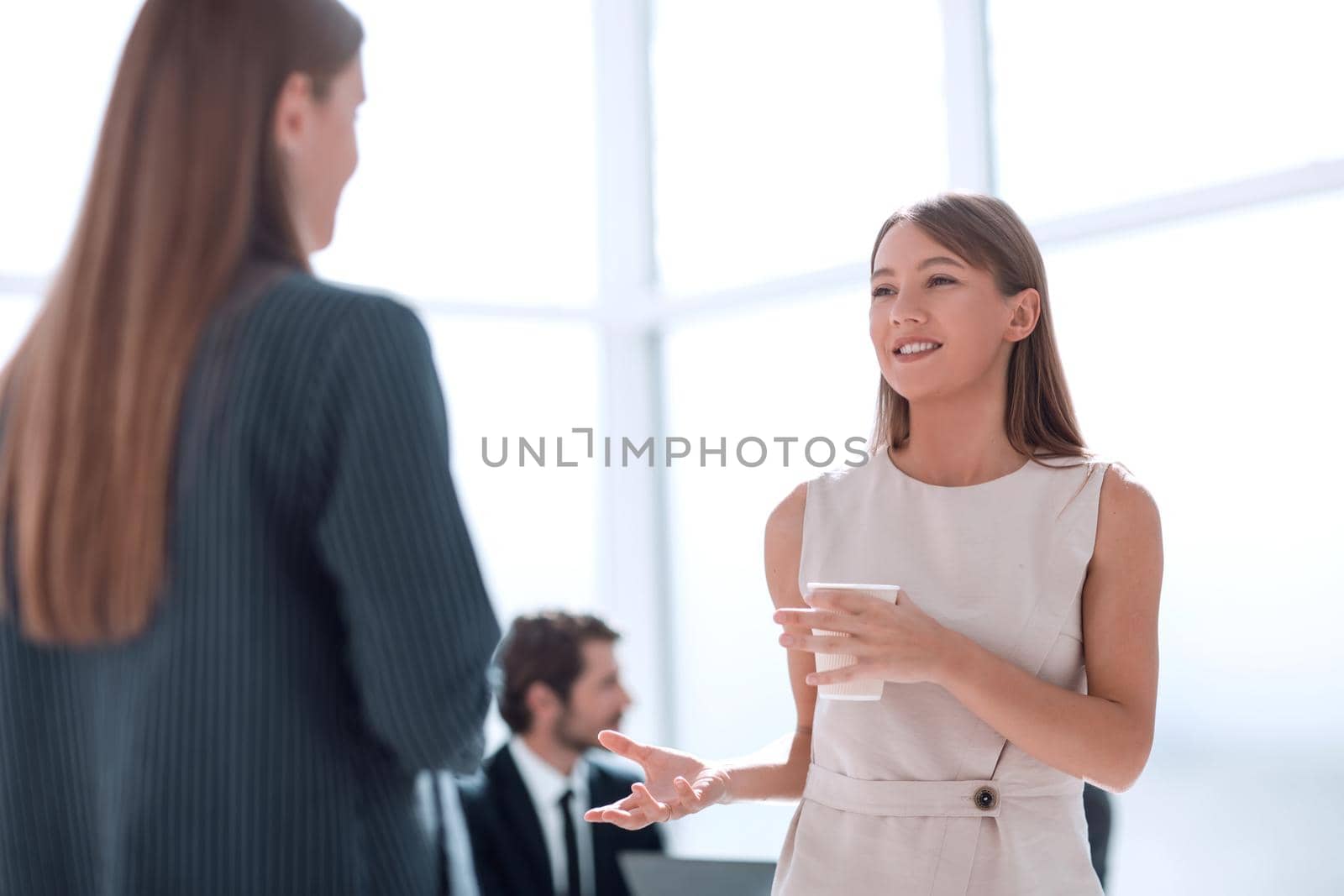 young businesswoman with a glass of coffee discussing something with her colleague