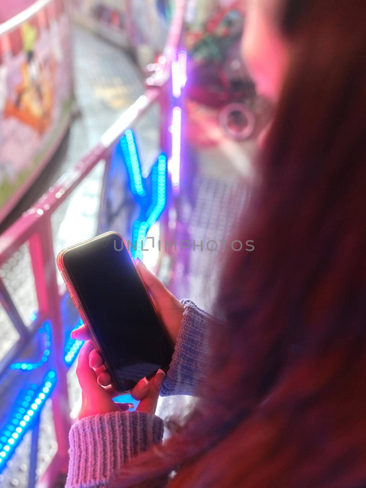 Vertical photo of the hands of a woman holding a mobile in a night fair by WesternExoticStockers