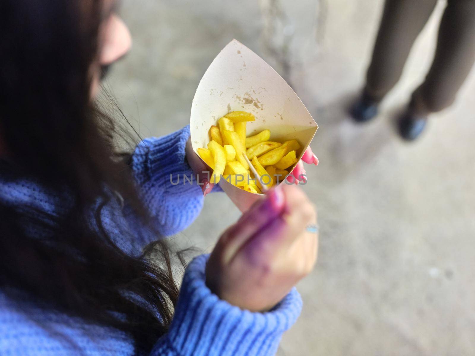 Top view and selective focus on the hands of a woman holding a french fries paper tin at a fair