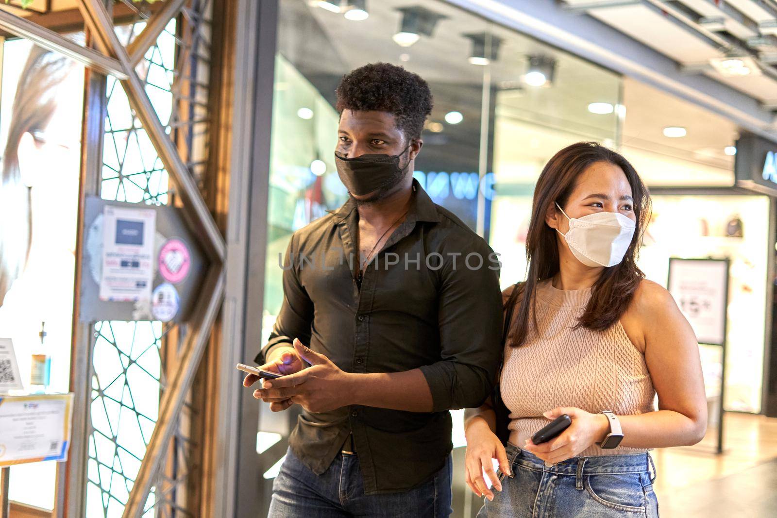 African man and asian woman with facial mask walking in a shopping mall