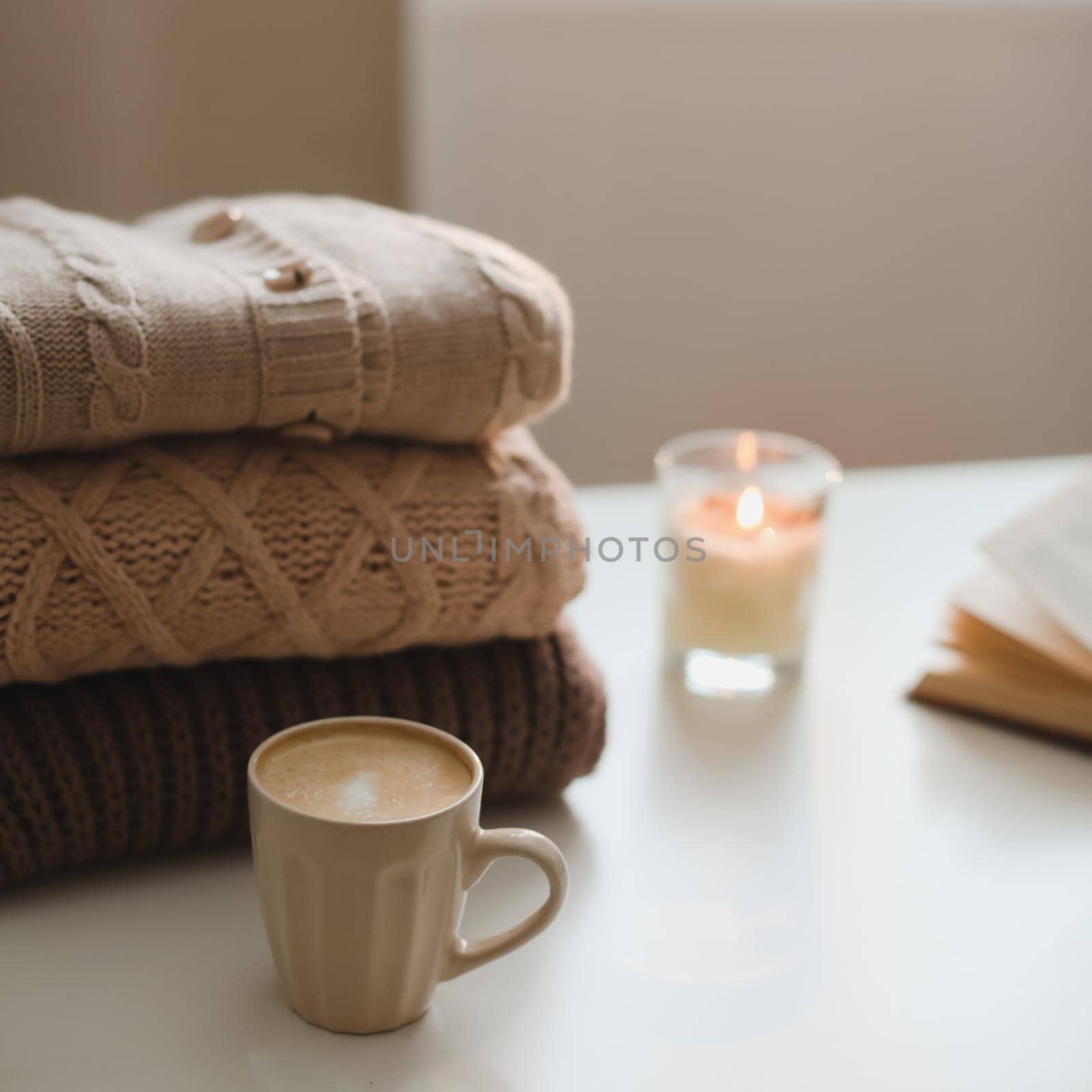 cozy home atmosphere and still life with candle and sweaters on a table.