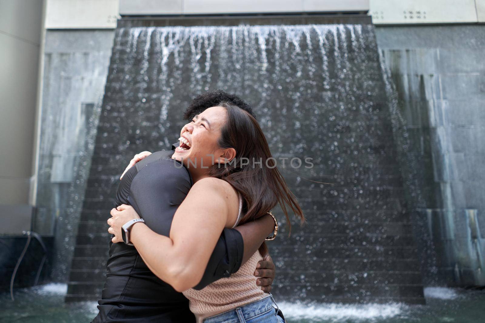 Close up portrait of multiethnic friends embracing next to an artificial waterfall in a modern mall