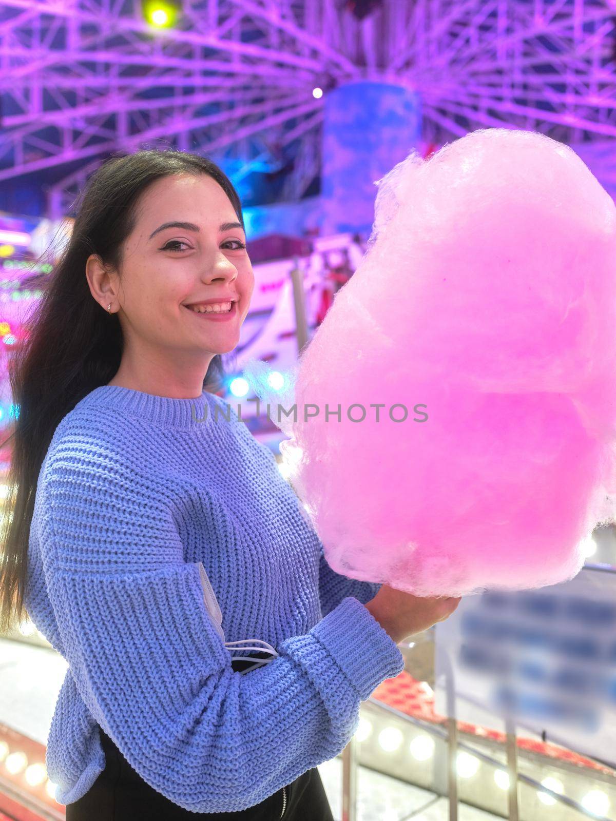 Vertical portrait of a smiling latina holding a cotton candy during a night fair