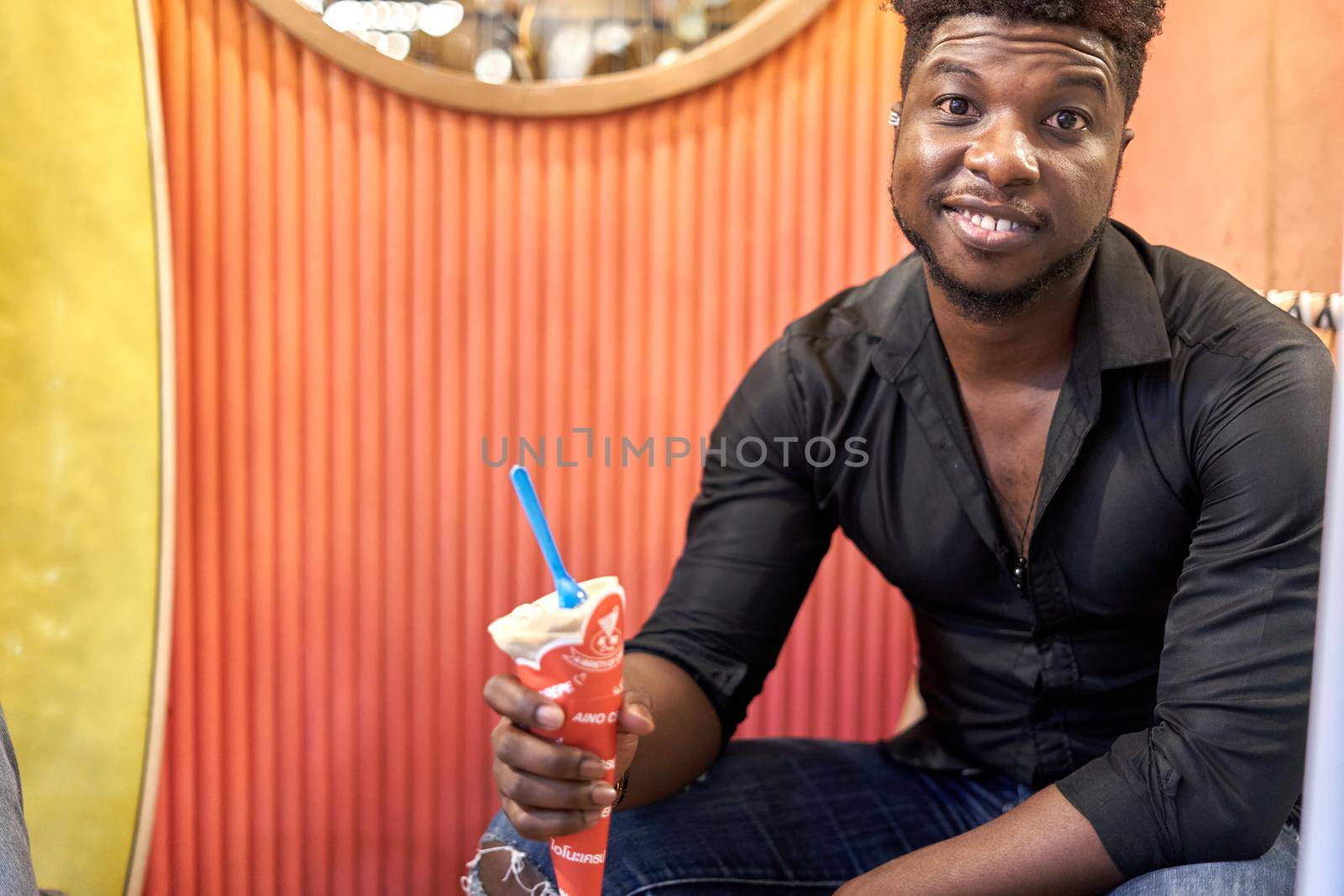 Portrait of a smiling african man eating ice cream while sitting on a shopping center