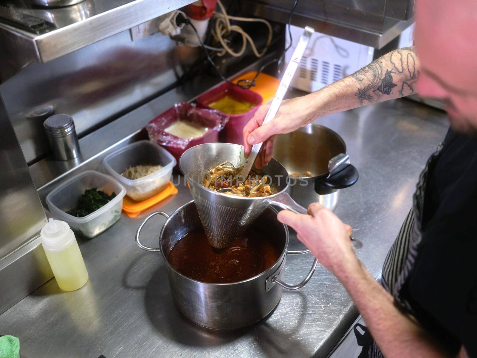 Chef strains food using a strainer in a pot to prepare a tasting menu in the kitchen of a restaurant