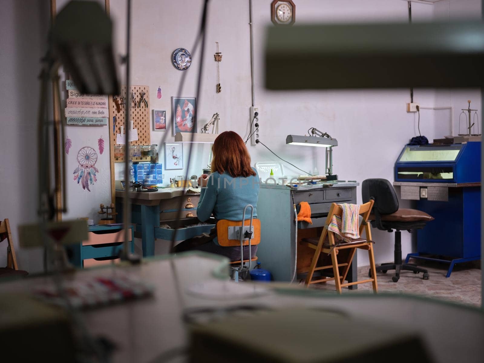 Rear view of an adult worker woman working in her jewelry artisan workshop sitting on workbench.