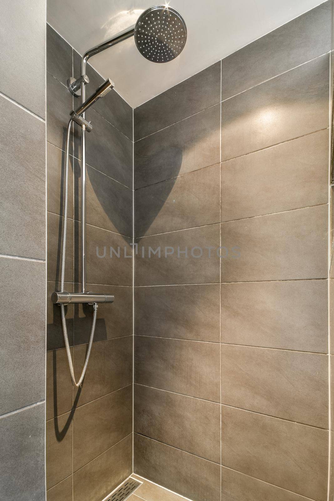 Shower faucets attached to tiled wall near glass partition and ornamental curtail in washroom at home