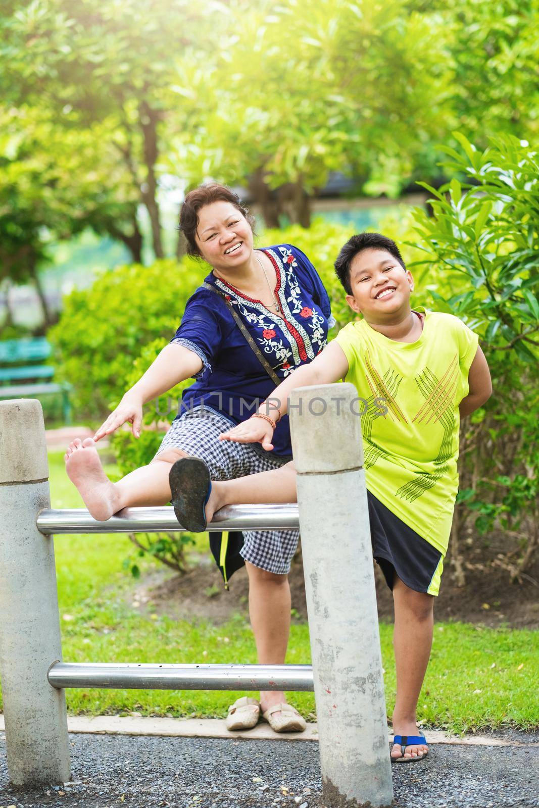Portrait Asian mother and son exercise in the garden.Sporty woman and child stretch practice in the public park.Outdoor relaxation and happiness family time concept. by Benzoix