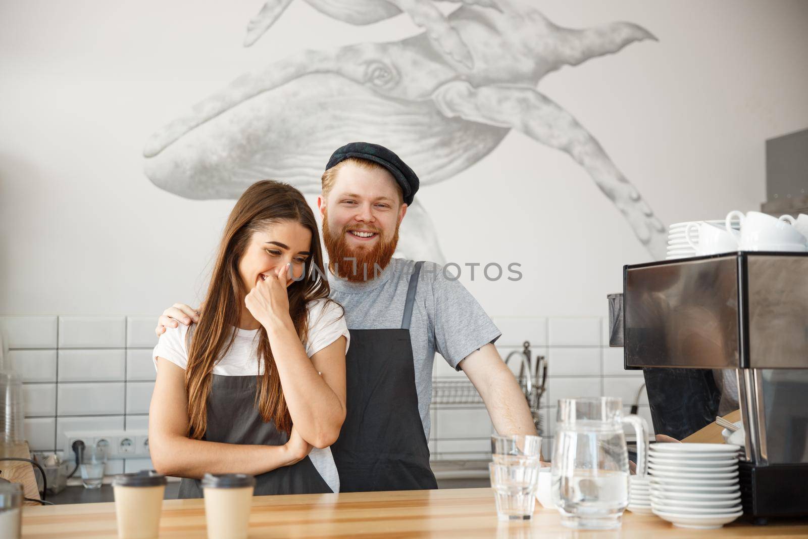 Coffee Business Concept - Positive young bearded man and beautiful attractive lady barista couple enjoy working together at the modern coffee shop