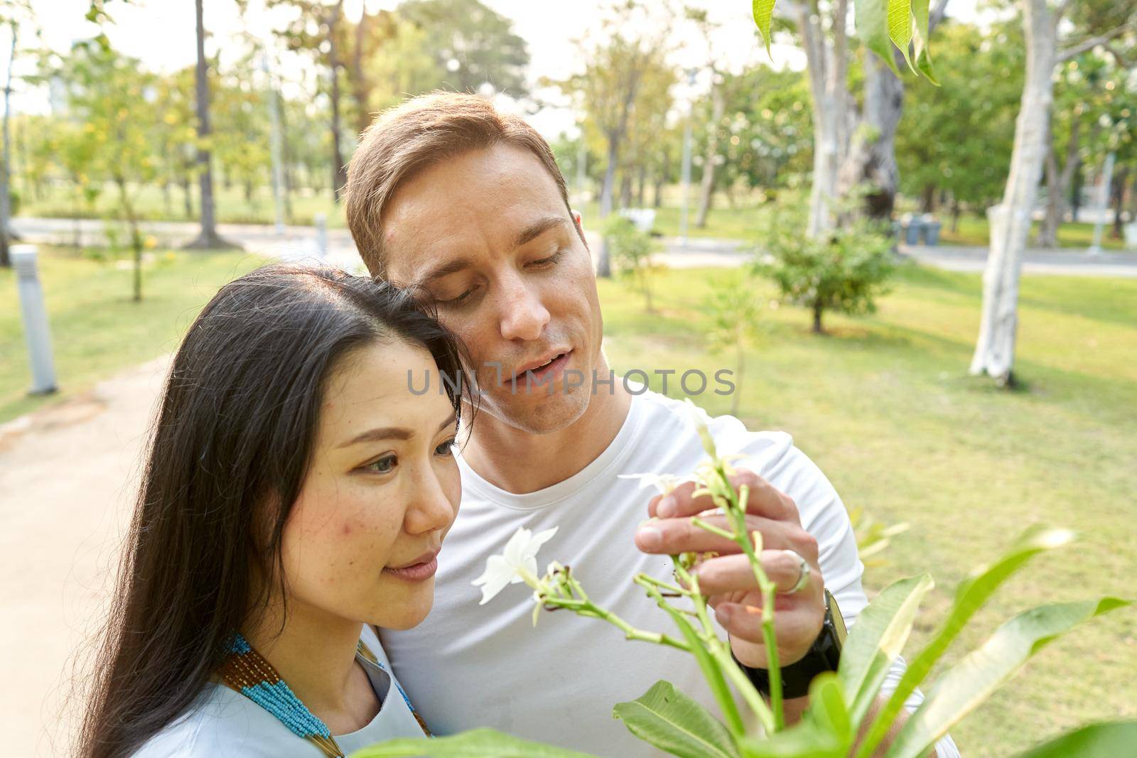 Multicultural couple looking and picking white flowers in an urban park by WesternExoticStockers