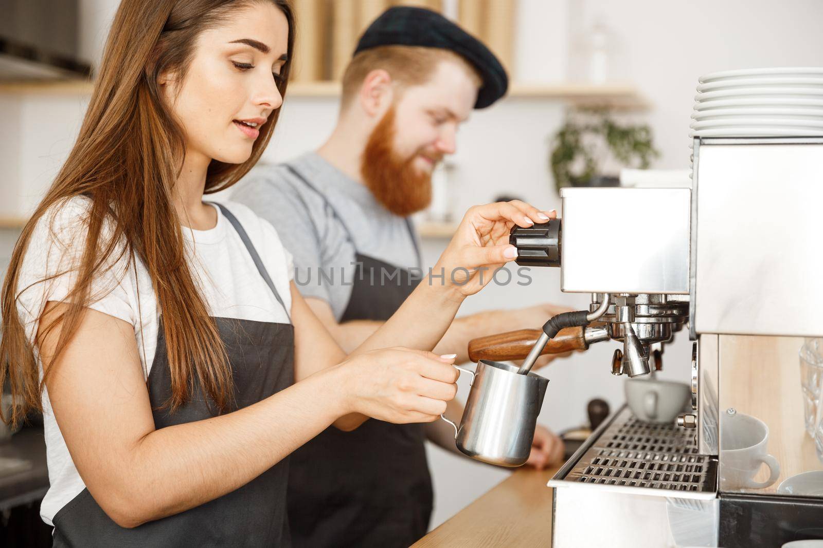 Coffee Business Concept - portrait of lady barista in apron preparing and steaming milk for coffee order with her partner while standing at cafe. by Benzoix