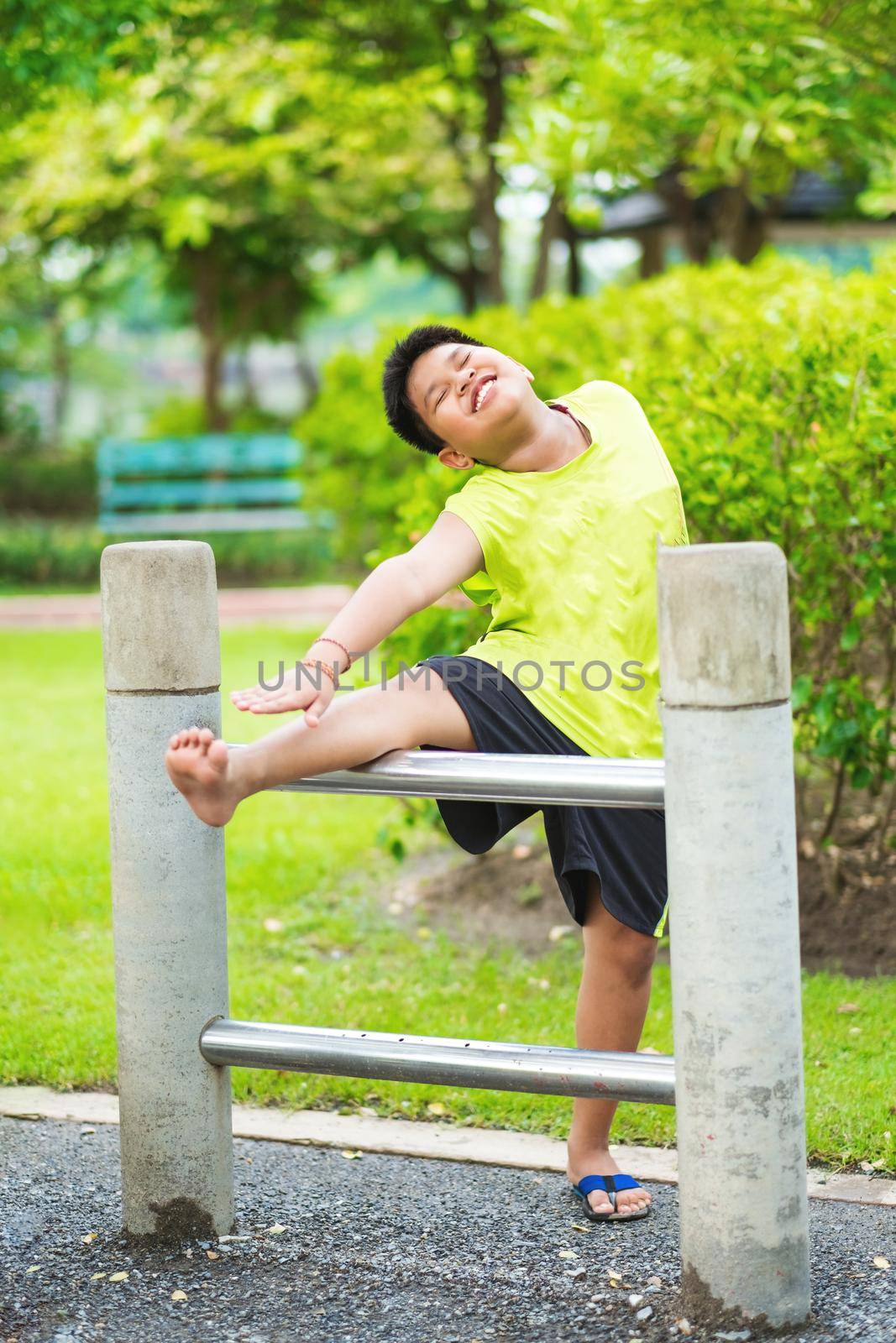Asian sport boy stretching on iron bar in garden.