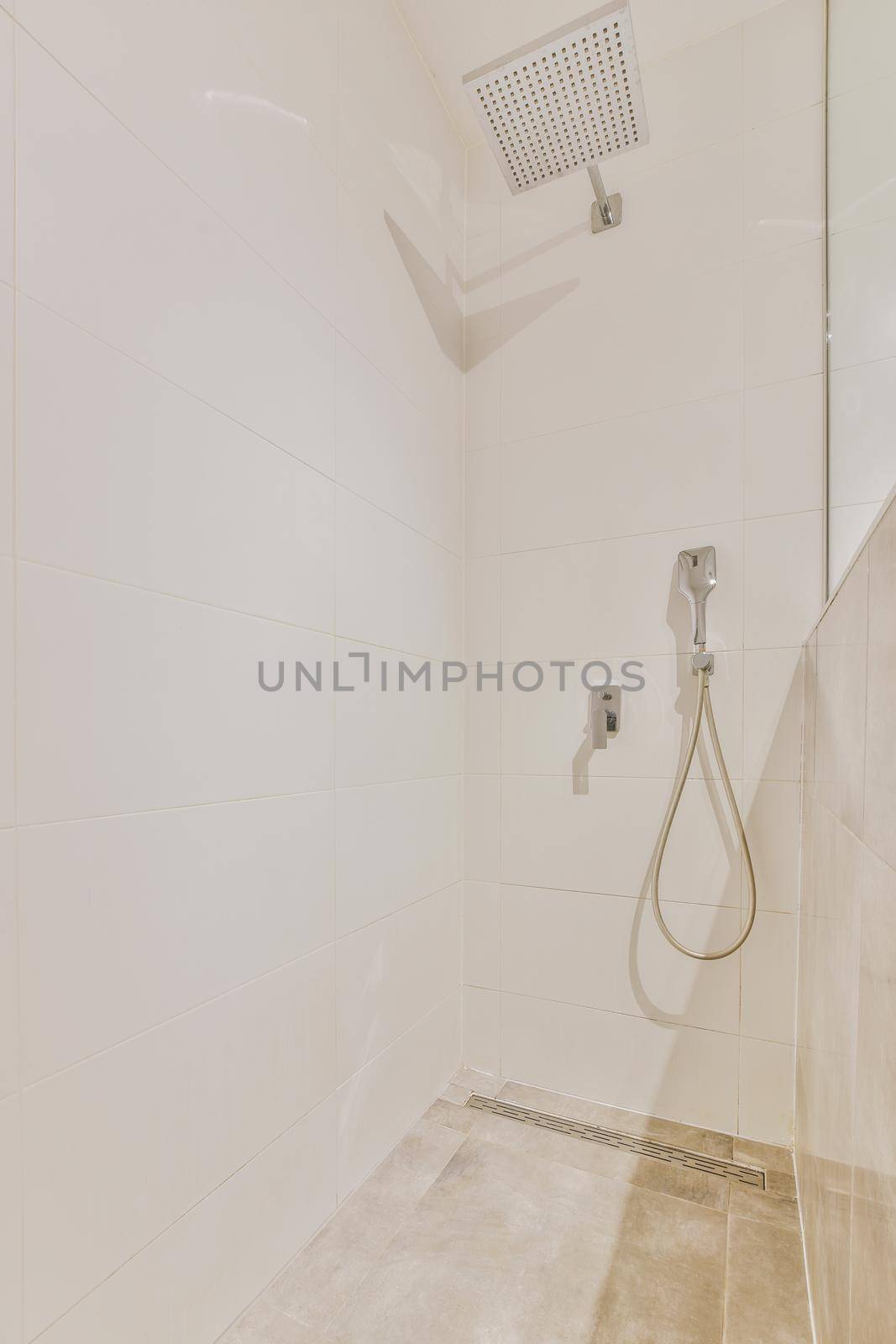 Shower faucets attached to tiled wall near glass partition and ornamental curtail in washroom at home