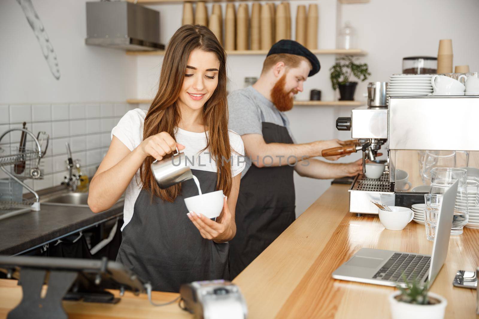 Coffee Business Concept - close-up lady barista in apron preparing and pouring milk into hot cup while standing at cafe.