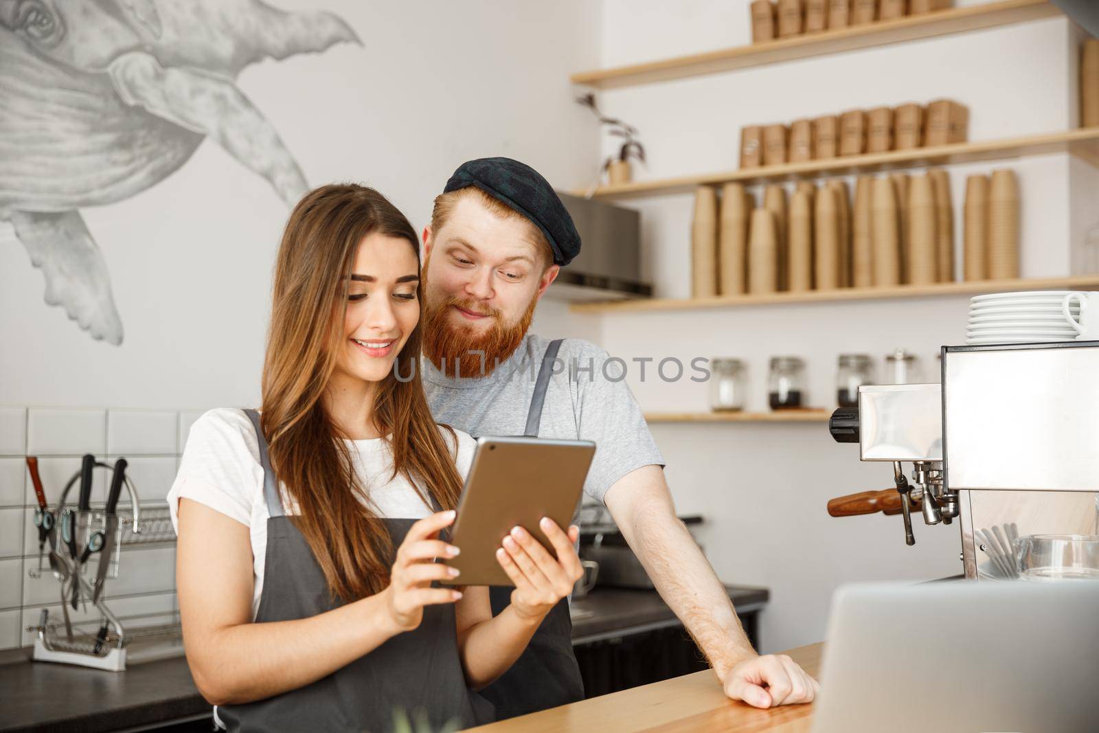 Coffee Business Concept - Satisfied and smile owners couple look on tablet orders online in modern coffee shop