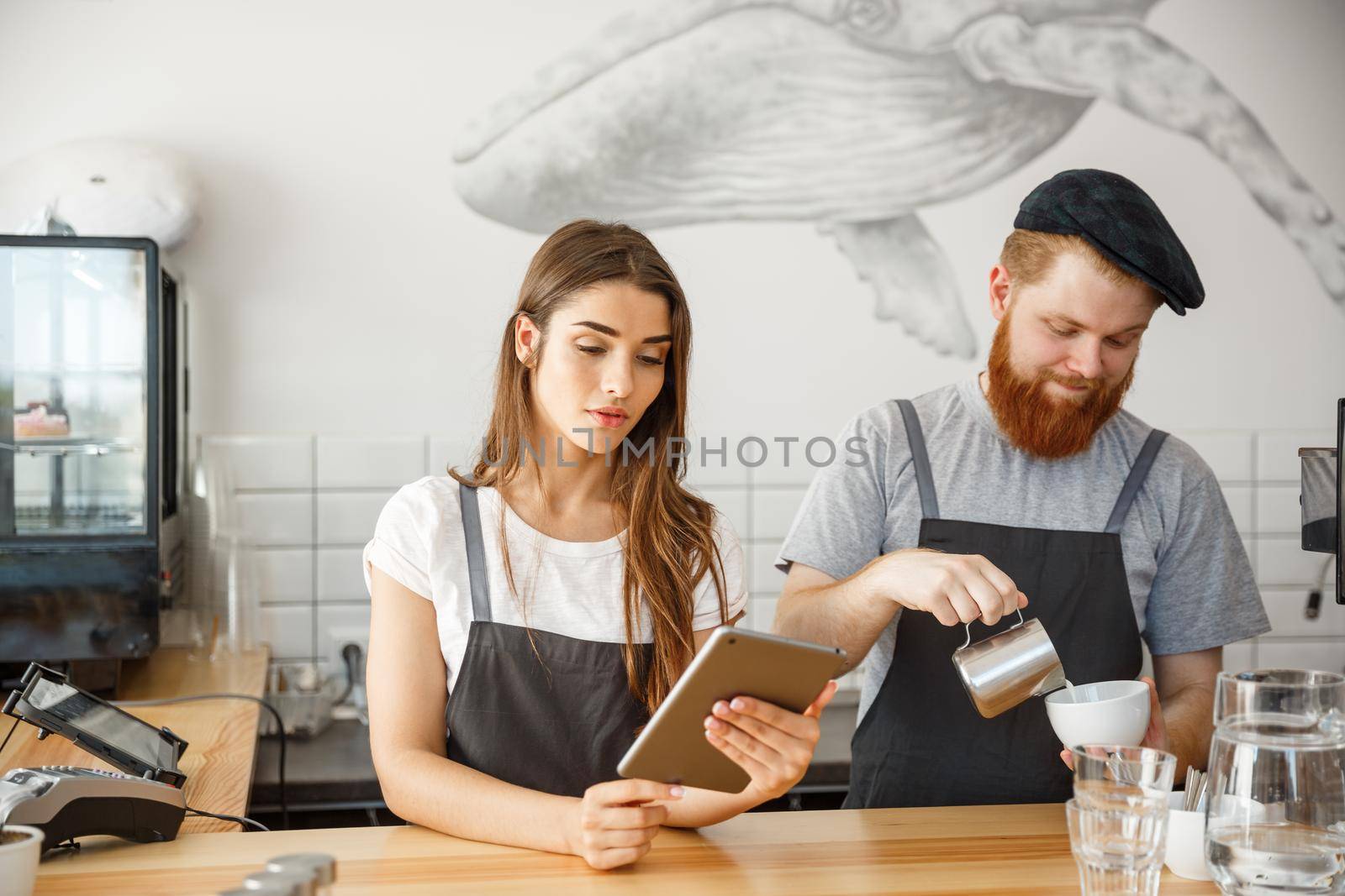 Coffee Business Concept - Cheerful baristas looking at their tablets for online orders in modern coffee shop.