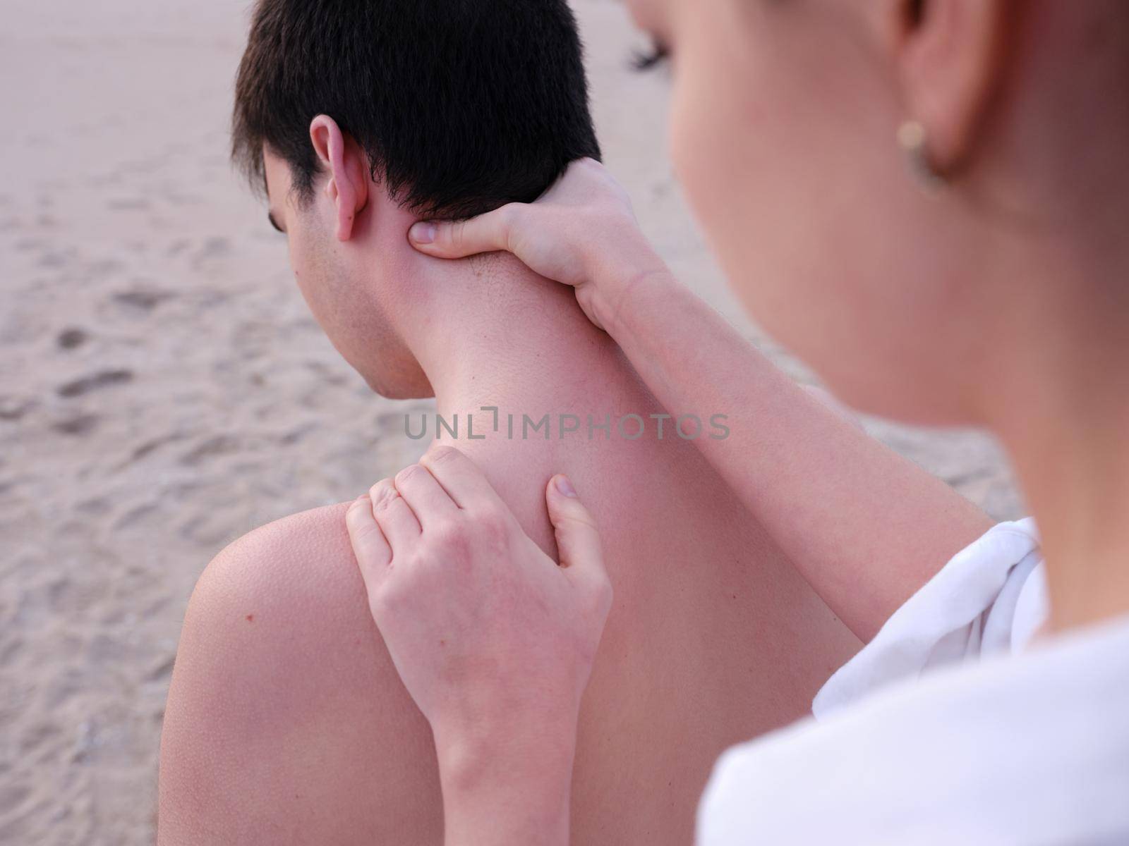 a young chiromassage therapist giving shoulder and neck massages to a young man on a beach in Valencia. by WesternExoticStockers