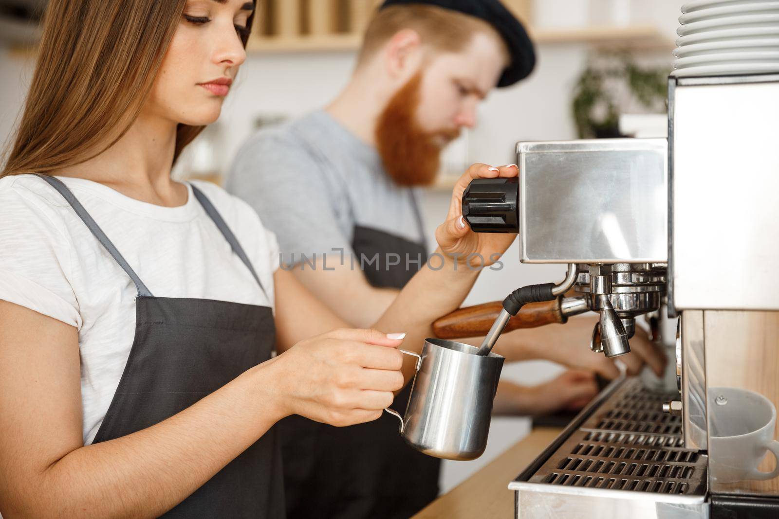 Coffee Business Concept - portrait of lady barista in apron preparing and steaming milk for coffee order with her partner while standing at cafe. by Benzoix