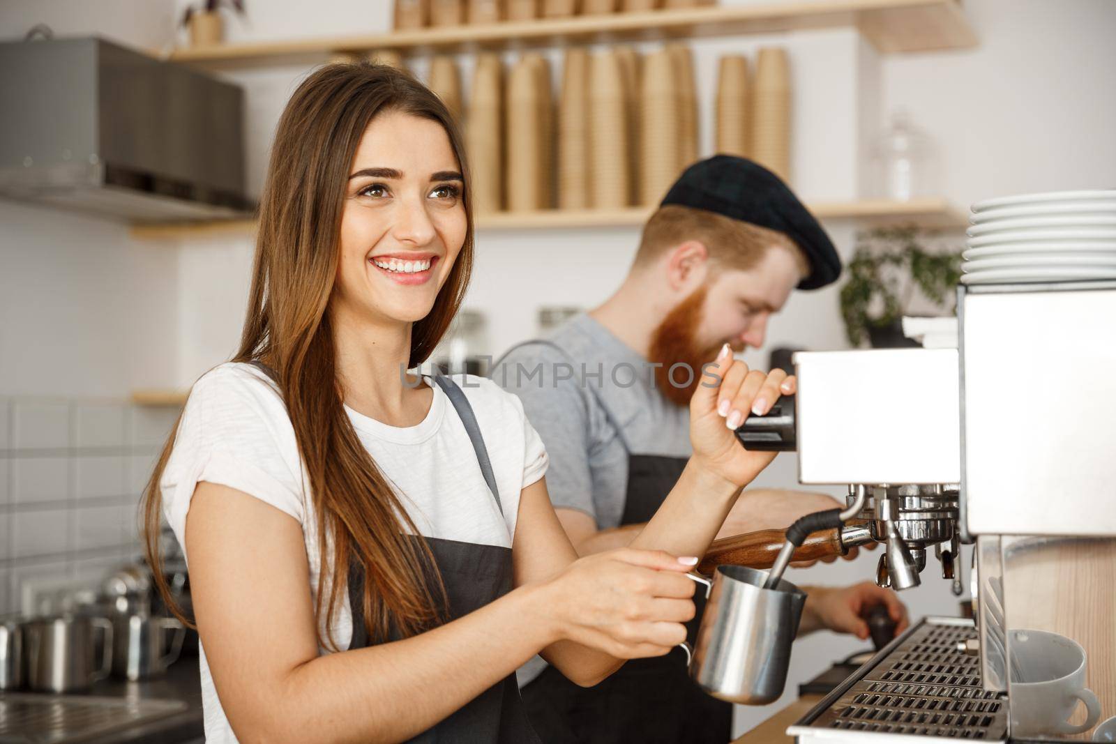 Coffee Business Concept - portrait of lady barista in apron preparing and steaming milk for coffee order with her partner while standing at cafe.