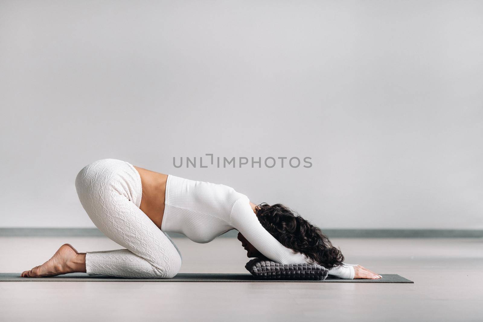 A woman doing yoga on a mat, kneeling makes a bow stretching her arms forward in the gym.