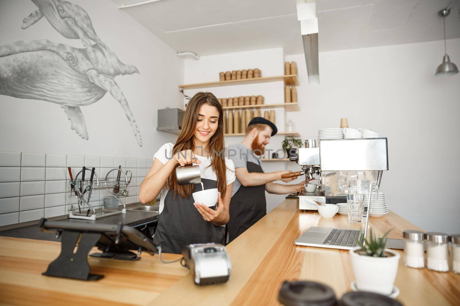 Coffee Business Concept - close-up lady barista in apron preparing and pouring milk into hot cup while standing at cafe.