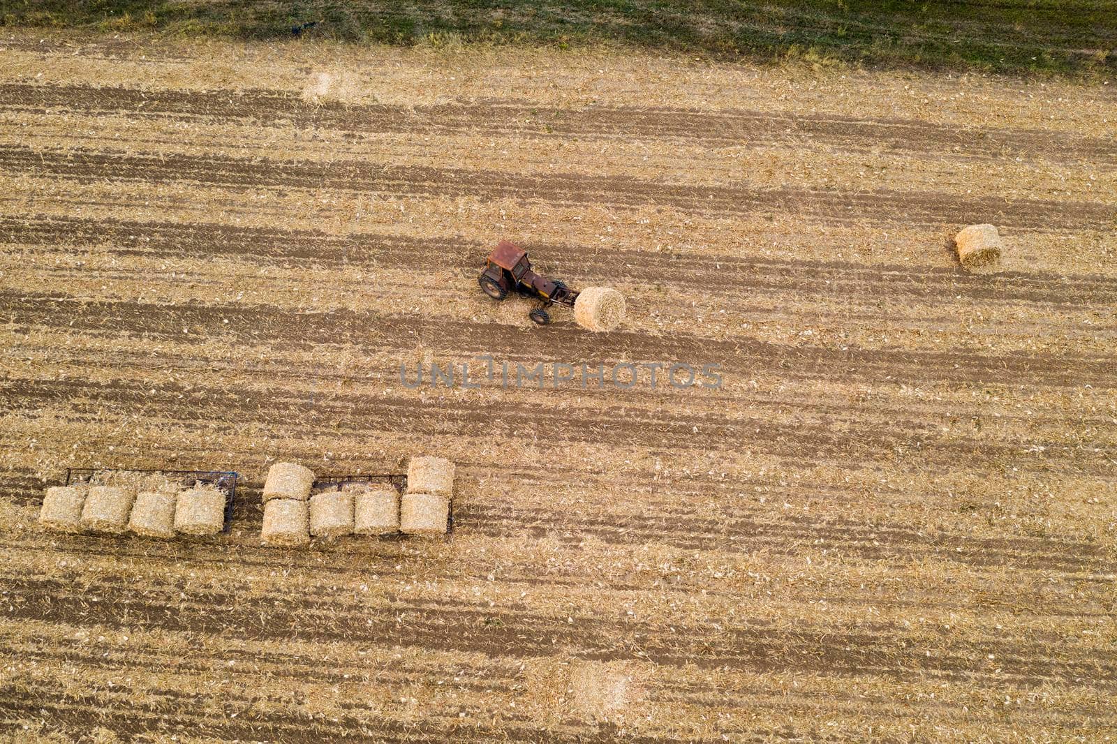 Aerial view from drone to the tractor collect bales of hay after harvesting on a wheat field.