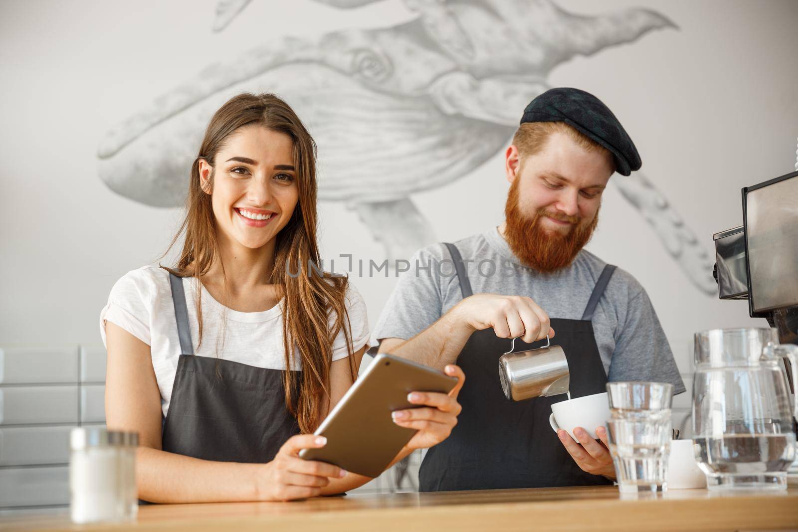 Coffee Business Concept - Cheerful baristas looking at their tablets for online orders in modern coffee shop. by Benzoix