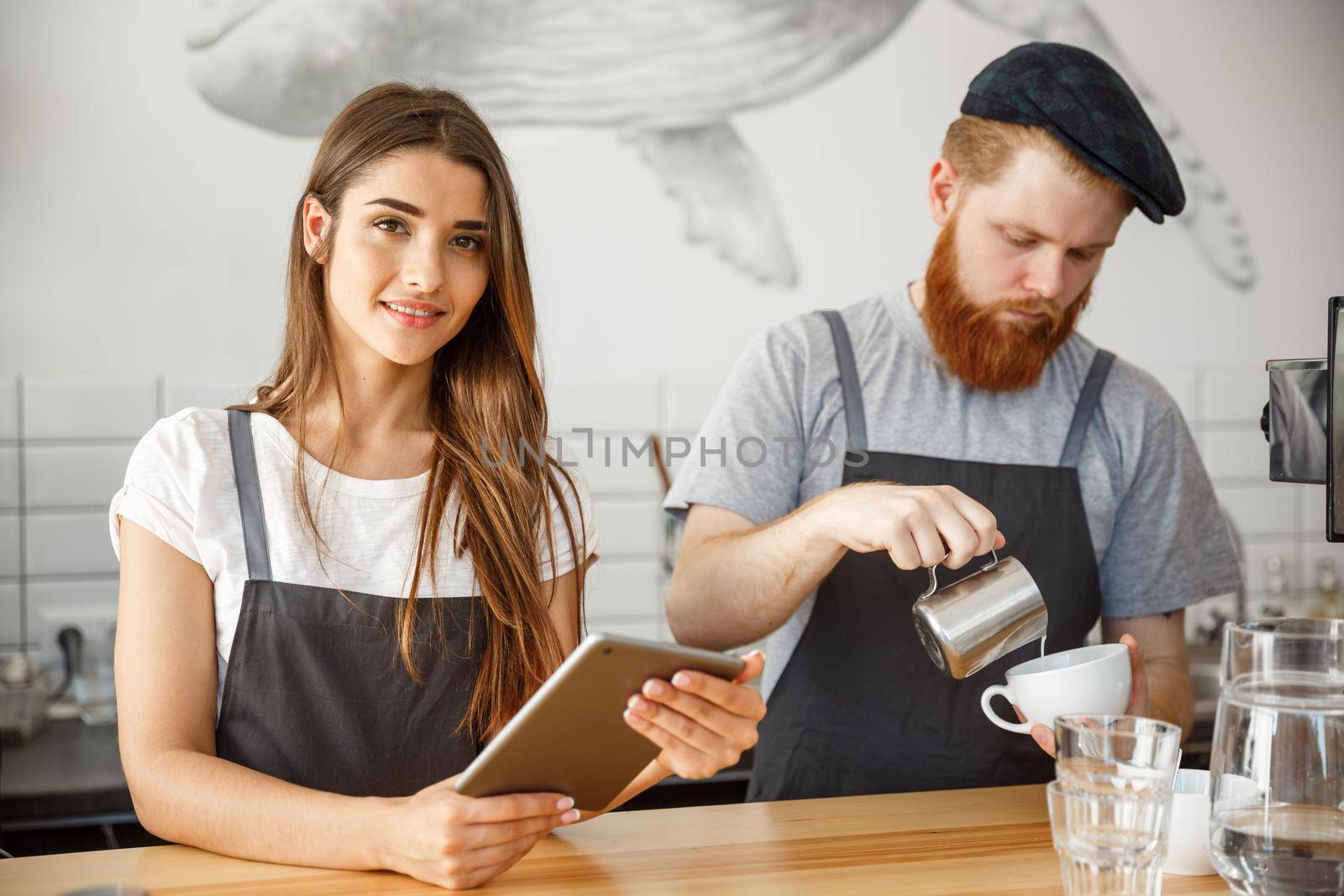 Coffee Business Concept - Cheerful baristas looking at their tablets for online orders in modern coffee shop.