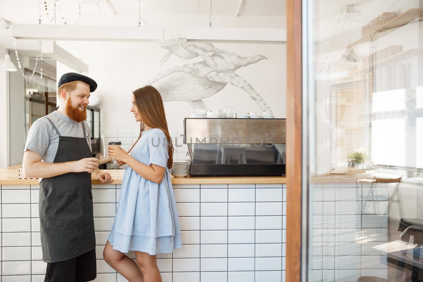 Coffee Business Concept - young smart bearded bartender enjoy talking and giving take away cup of coffee to pretty customer. by Benzoix