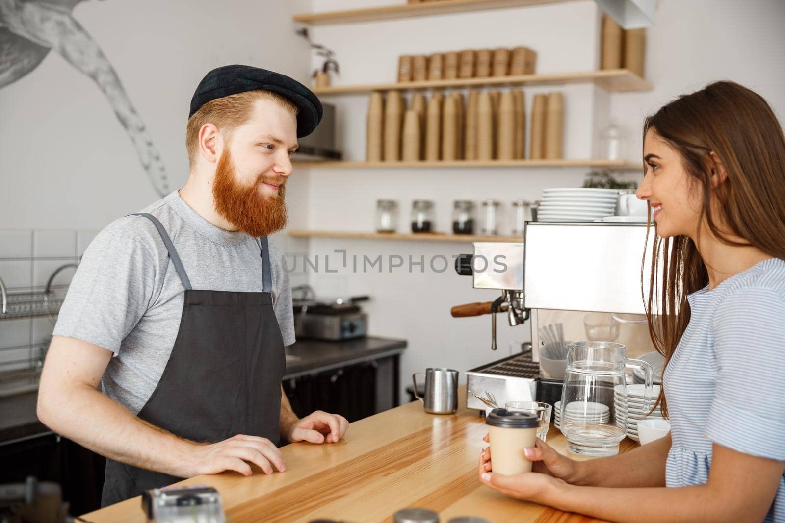 Coffee Business Concept - young beared handsome barista talking with beautiful caucasian customer in modern coffee shop.