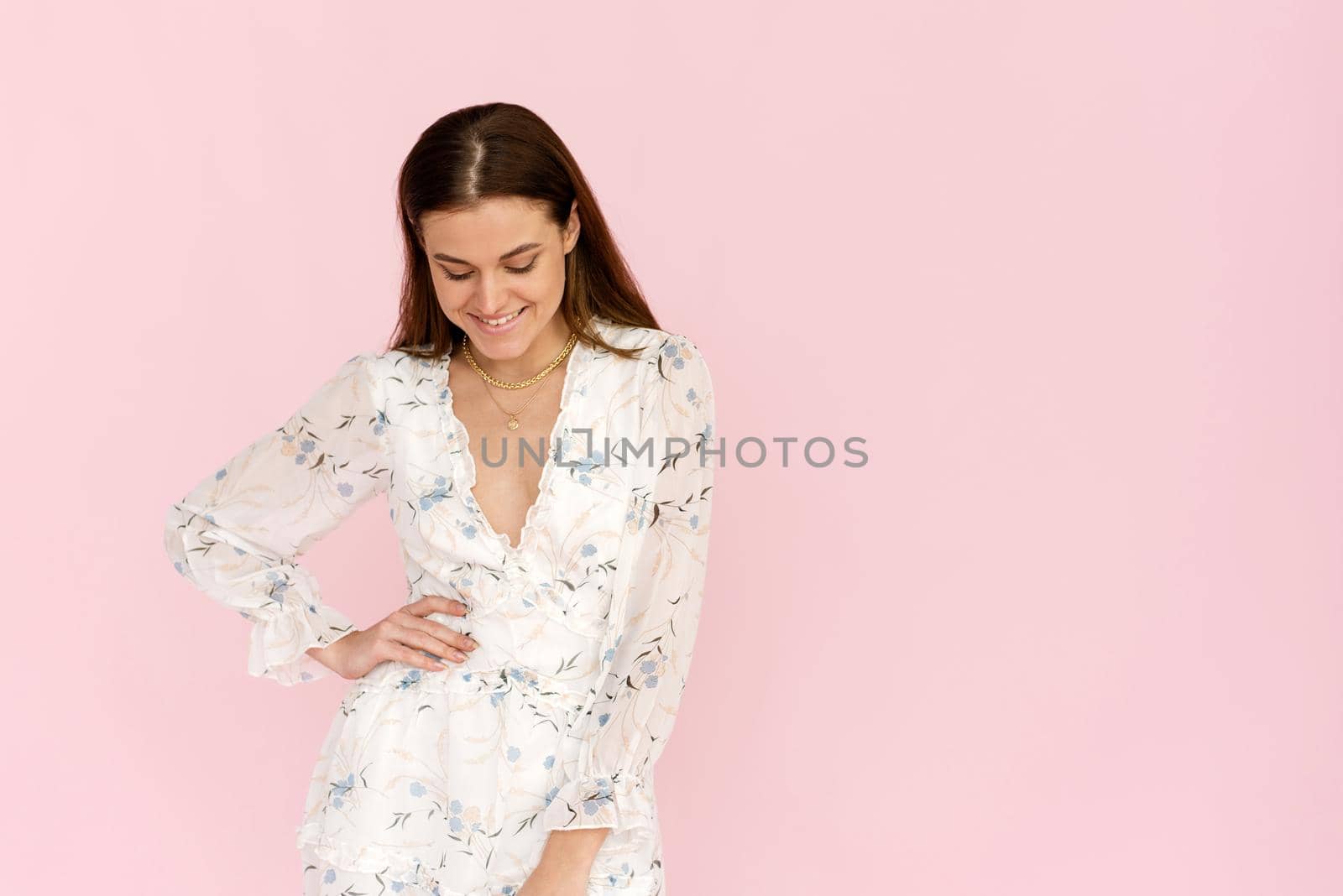 Beautiful smiling stylish woman in a white dress in a romantic mood posing on a pink background, summer fashion style