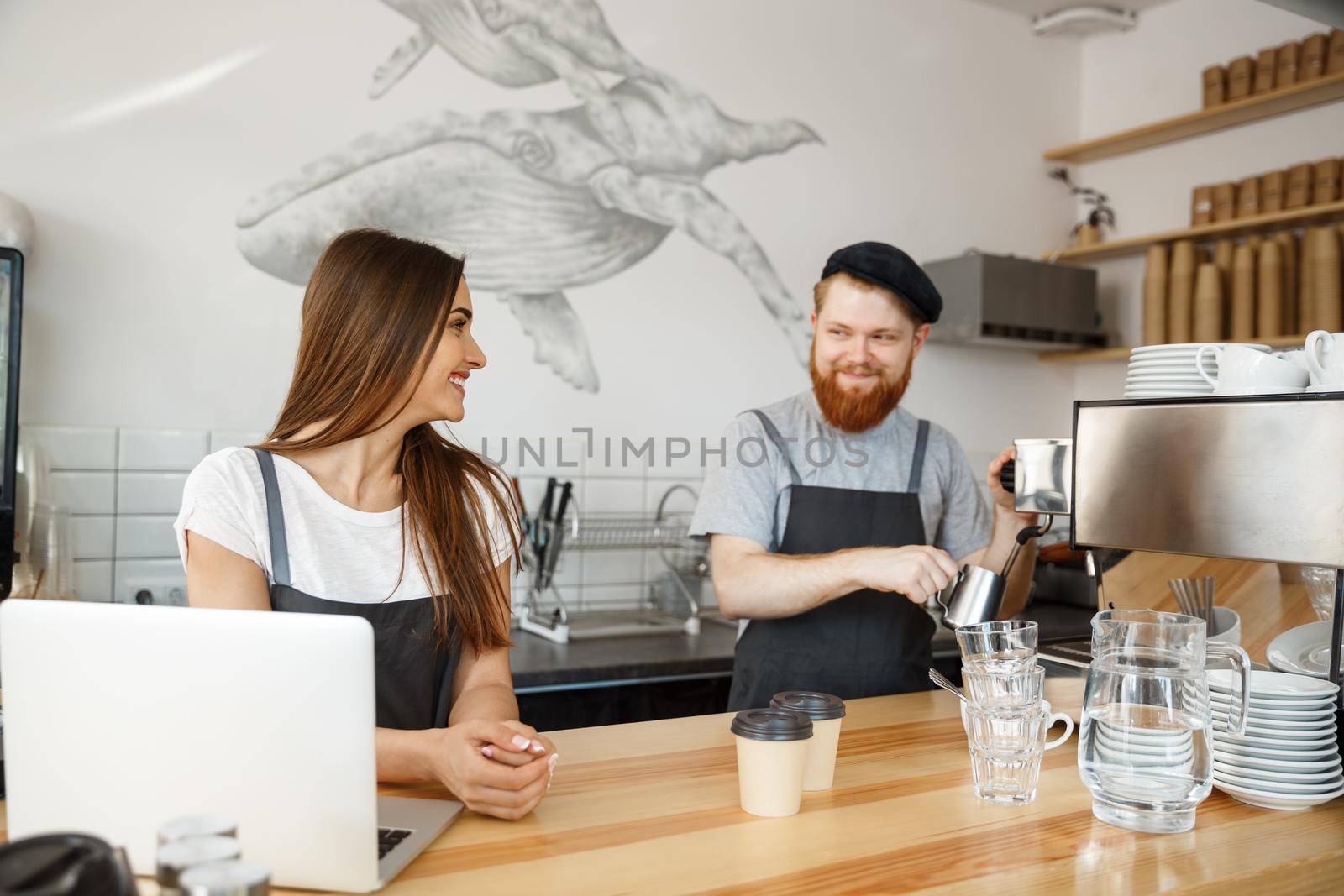 Coffee Business Concept - Positive young bearded man and beautiful attractive lady barista couple enjoy working together at the modern coffee shop by Benzoix