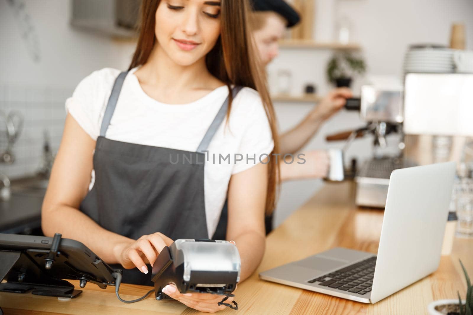 Coffee Business Concept - Beautiful female barista giving payment service for customer with credit card and smiling while working at the bar counter in modern coffee shop. by Benzoix