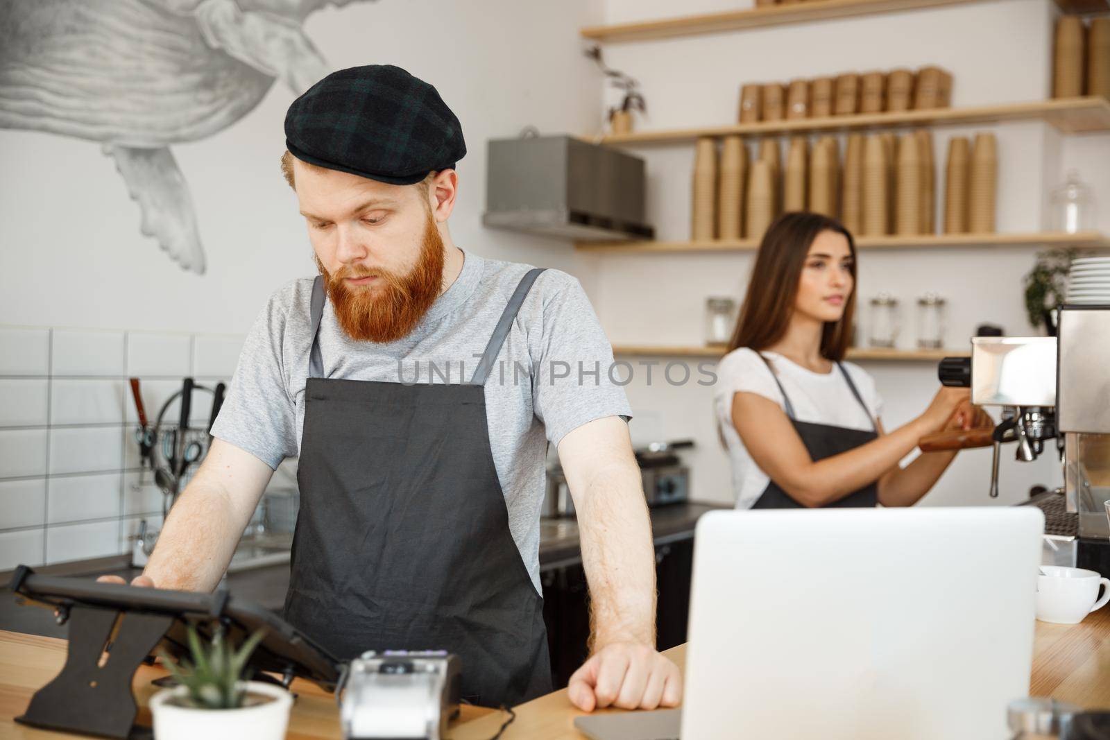 Coffee Business Concept - Young handsome bearded bartender, barista or manager posting the order from guest in digital tablet menu at modern coffee shop