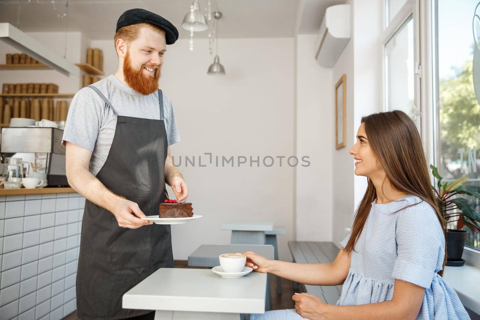 Coffee Business Concept - Waiter or bartender giving chocolate cake and talking with caucasian beautiful lady in blue dress at Coffee shop. by Benzoix