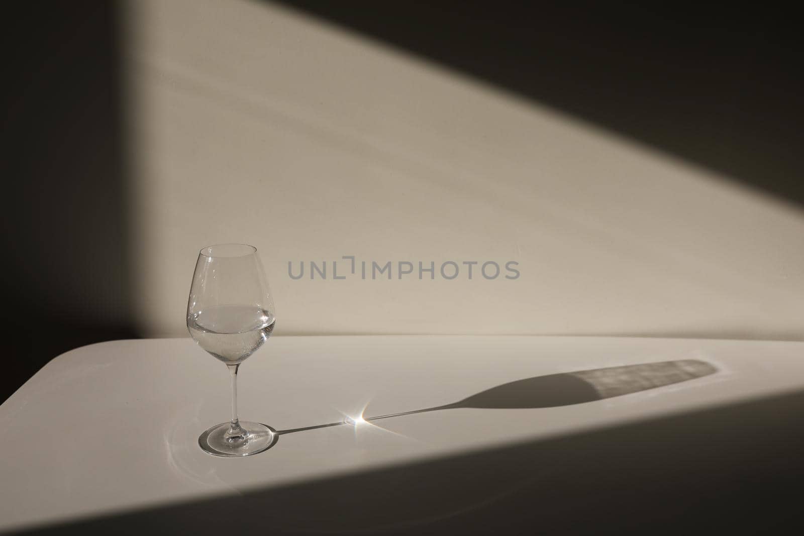 A glass of water on a white background with a shadow. Chiaroscuro from the window. Close-up, copy space.
