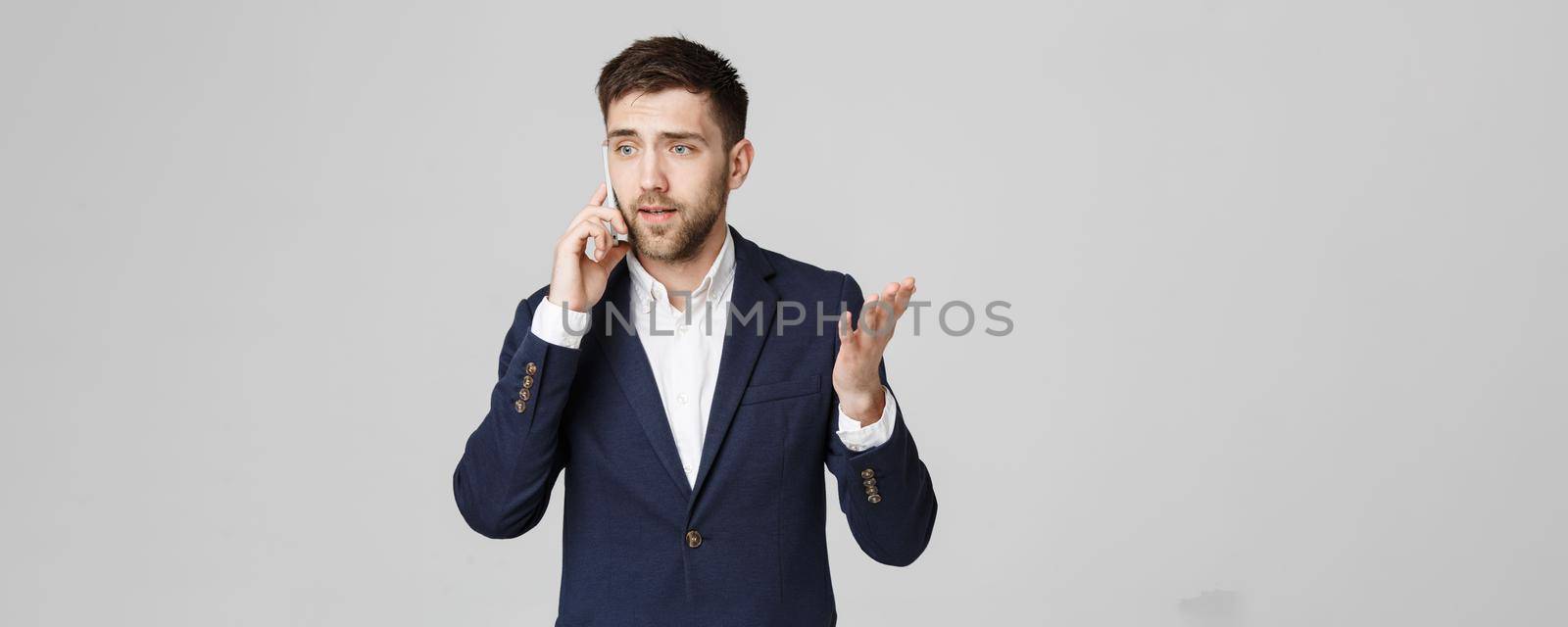 Business Concept - Portrait young handsome angry business man in suit talking on phone looking at camera. White background. by Benzoix